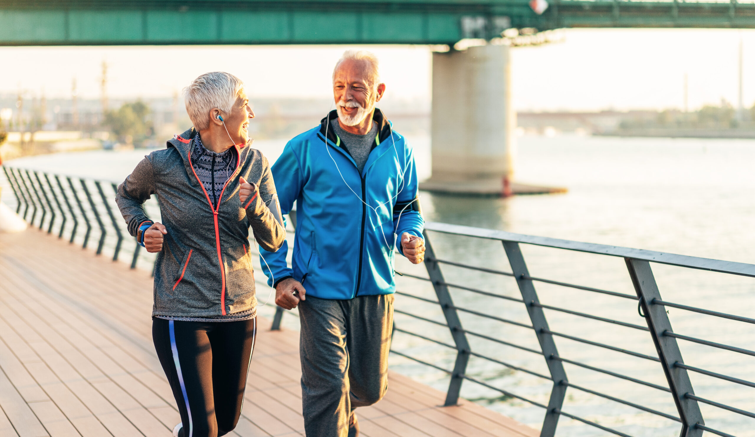 A retired couple jogging on a waterfront walkway along a river.